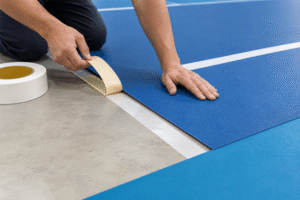 Worker installing blue pickleball court flooring with double sided tape